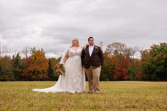 Couple poses in color autumn field at private family camp Charleston, Maine fall wedding